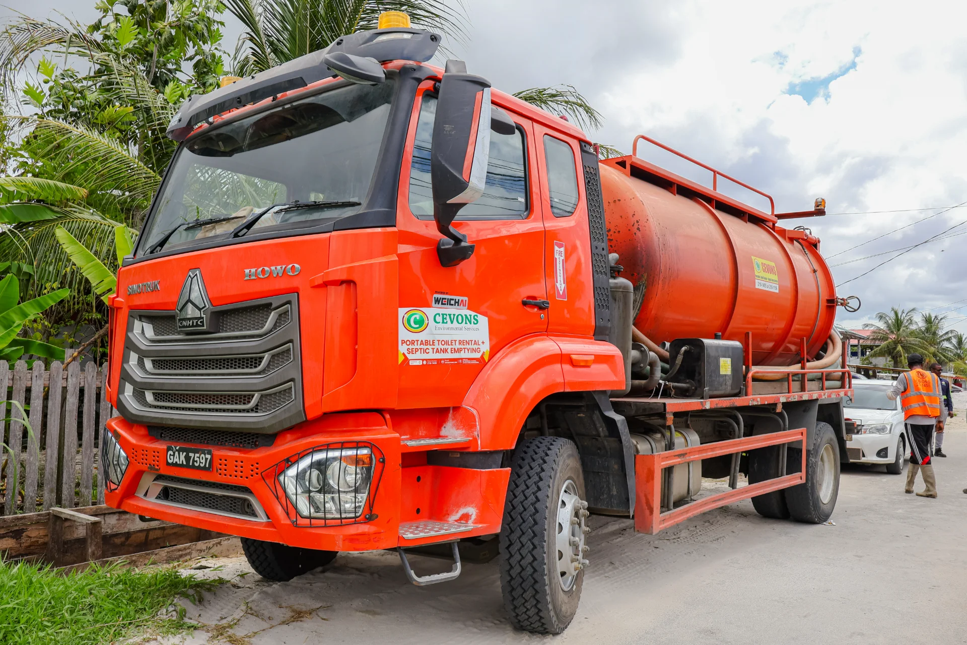Orange CEVONS Sinotruk HOWO vacuum tanker truck parked on a sand road beside a wooden fence, signwritten for portable toilet rental and septic tank emptying.